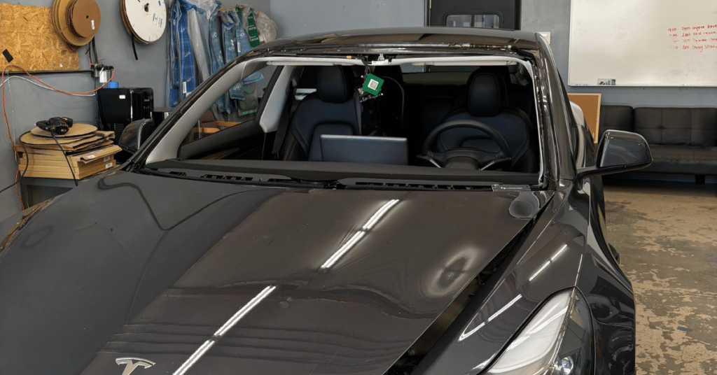 Black Tesla with its windshield removed in a repair shop, awaiting auto window tint.
