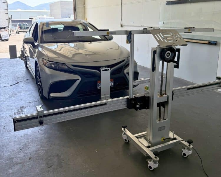 A silver sedan parked in an auto repair shop with a professional wheel alignment and ADAS calibration frame positioned in front of it.