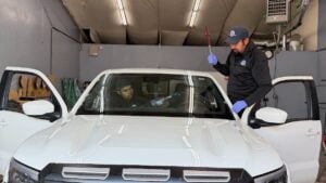 Two workers clean the interior windshield of a white SUV inside a garage; one sprays, while the other uses a tool on the glass, ensuring every detail is spotless for optimal visibility and lasting auto glass protection.