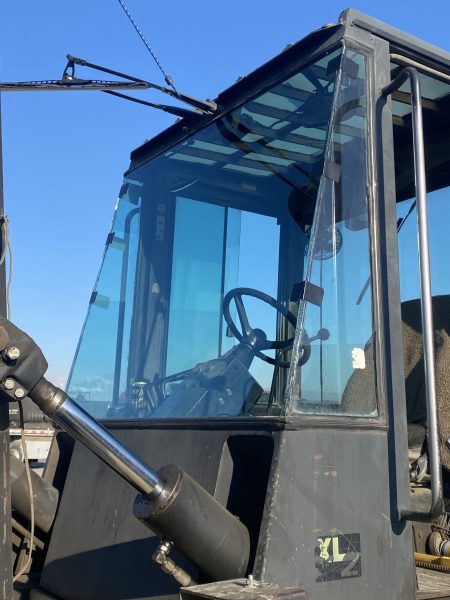 Close-up of a construction vehicle cabin with a steering wheel, hydraulic controls, and clear blue sky in the background.