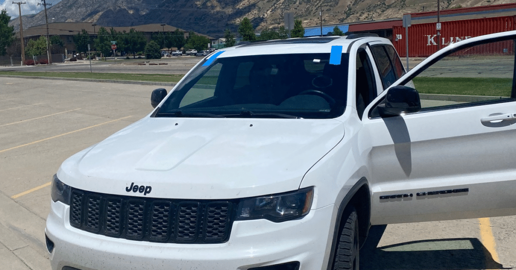 White Jeep Grand Cherokee with the driver-side door open and blue painter’s tape on the windshield during the car window tinting process.