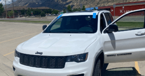 White Jeep Grand Cherokee with the driver-side door open and blue painter’s tape on the windshield during the car window tinting process.