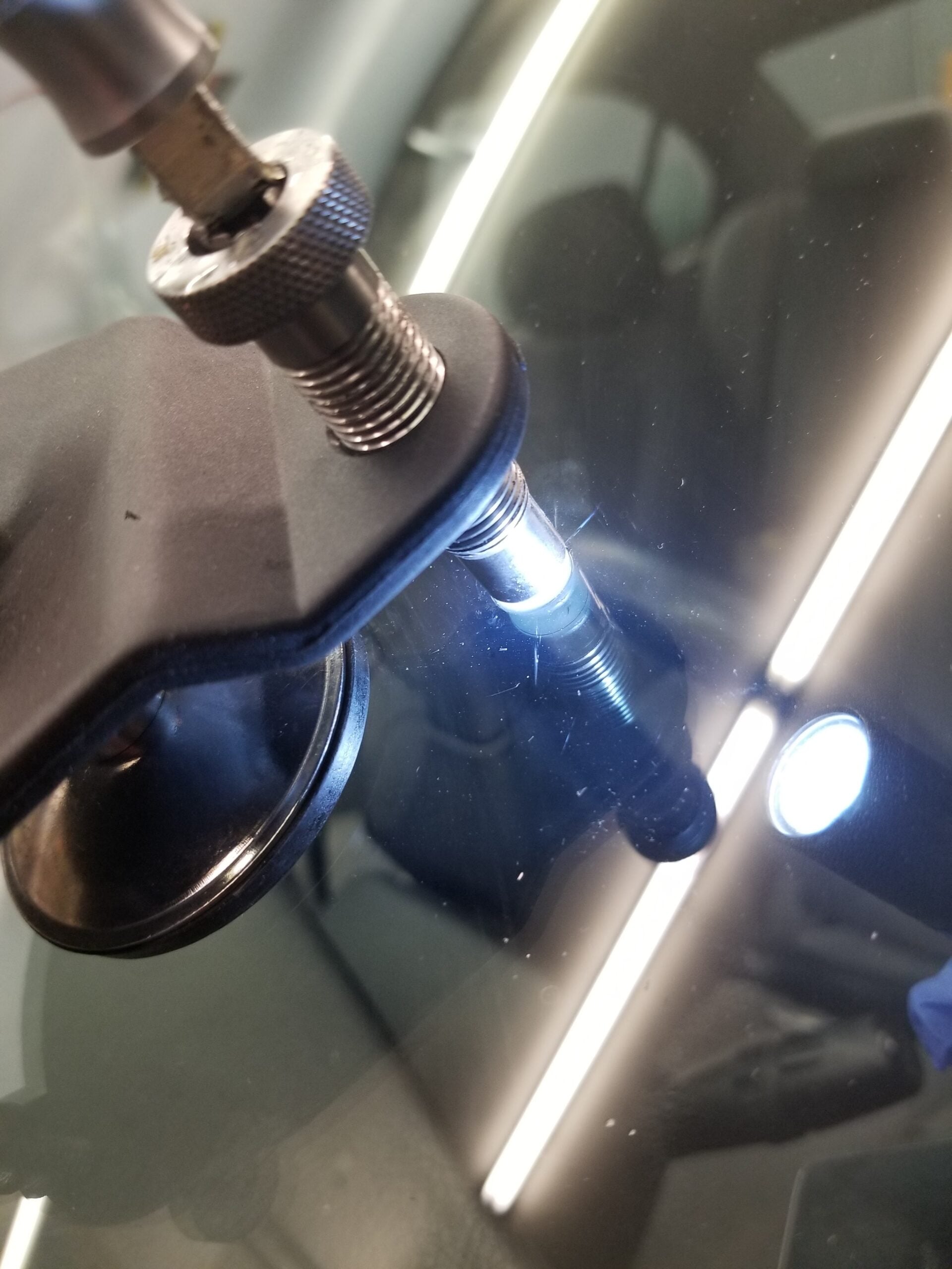 Close-up of a windshield repair tool with a bright light illuminating a chip or crack in the glass.
